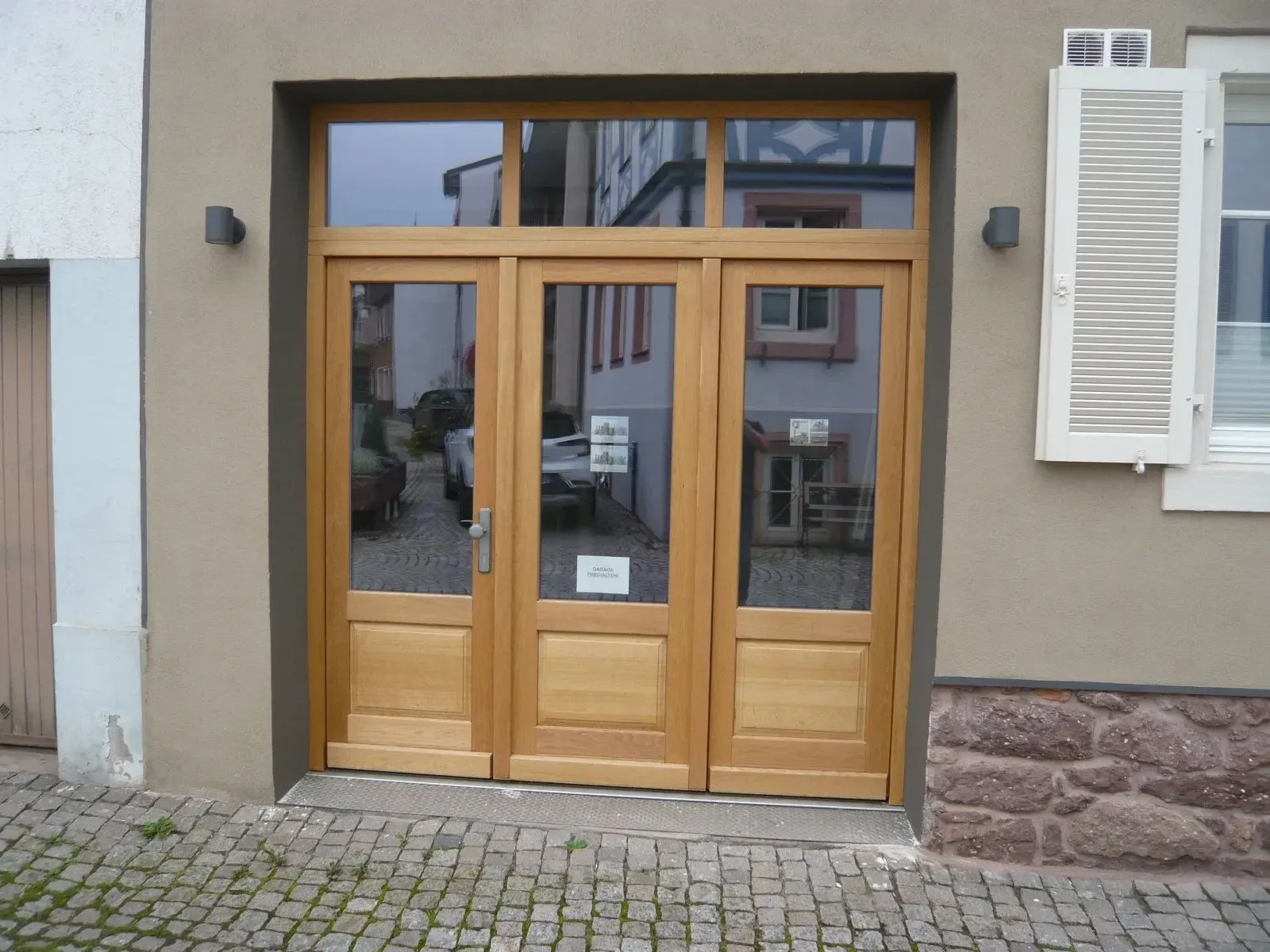 Dreiteilige Eingangstür aus Eiche mit Glasfeldern und Oberlicht in einer verputzten Fassade
