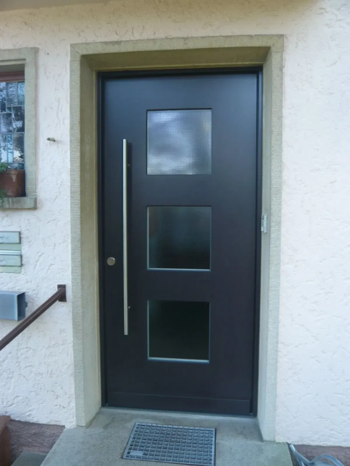 Moderne anthrazitfarbene Haustür mit drei Glaseinsätzen und langem Edelstahlgriff