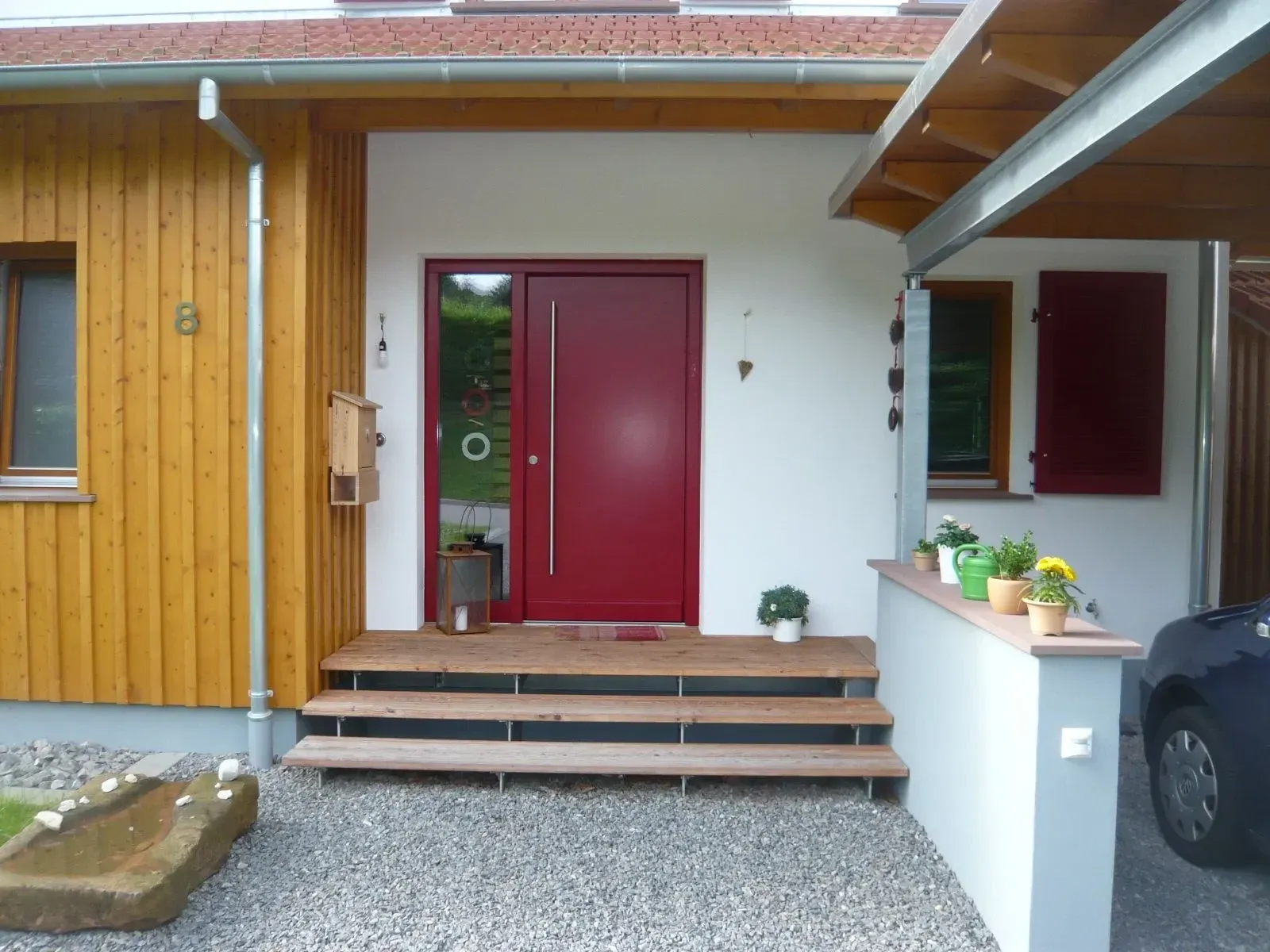 Rote Haustür mit Seitenteil unter einem Vordach an einem Neubau mit Holzfassade