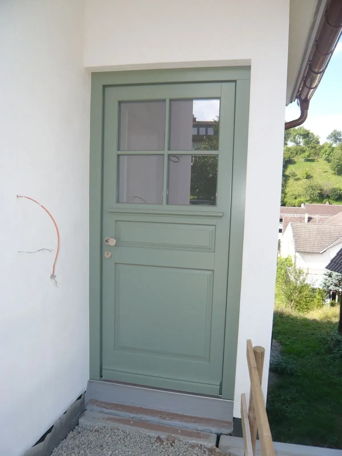 Salbeigrüne Holzhaustür mit Sprossenfenster und Kassette an einem weißen Wohnhaus