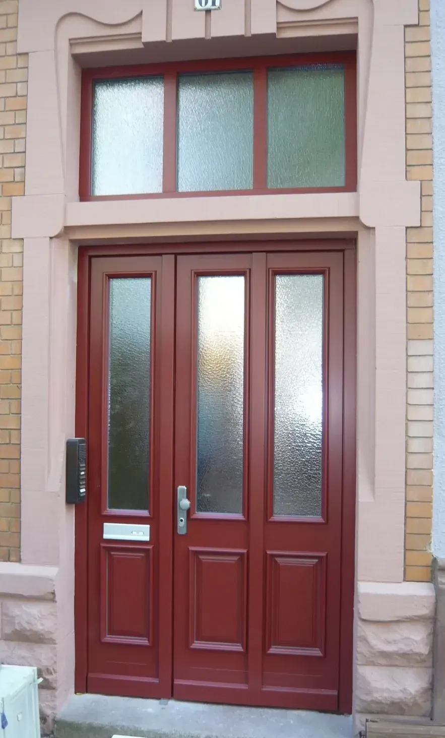 Zweiflügelige weinrote Haustür mit Ornamentglas und dreiteiligem Oberlicht in einer Sandsteinfassade