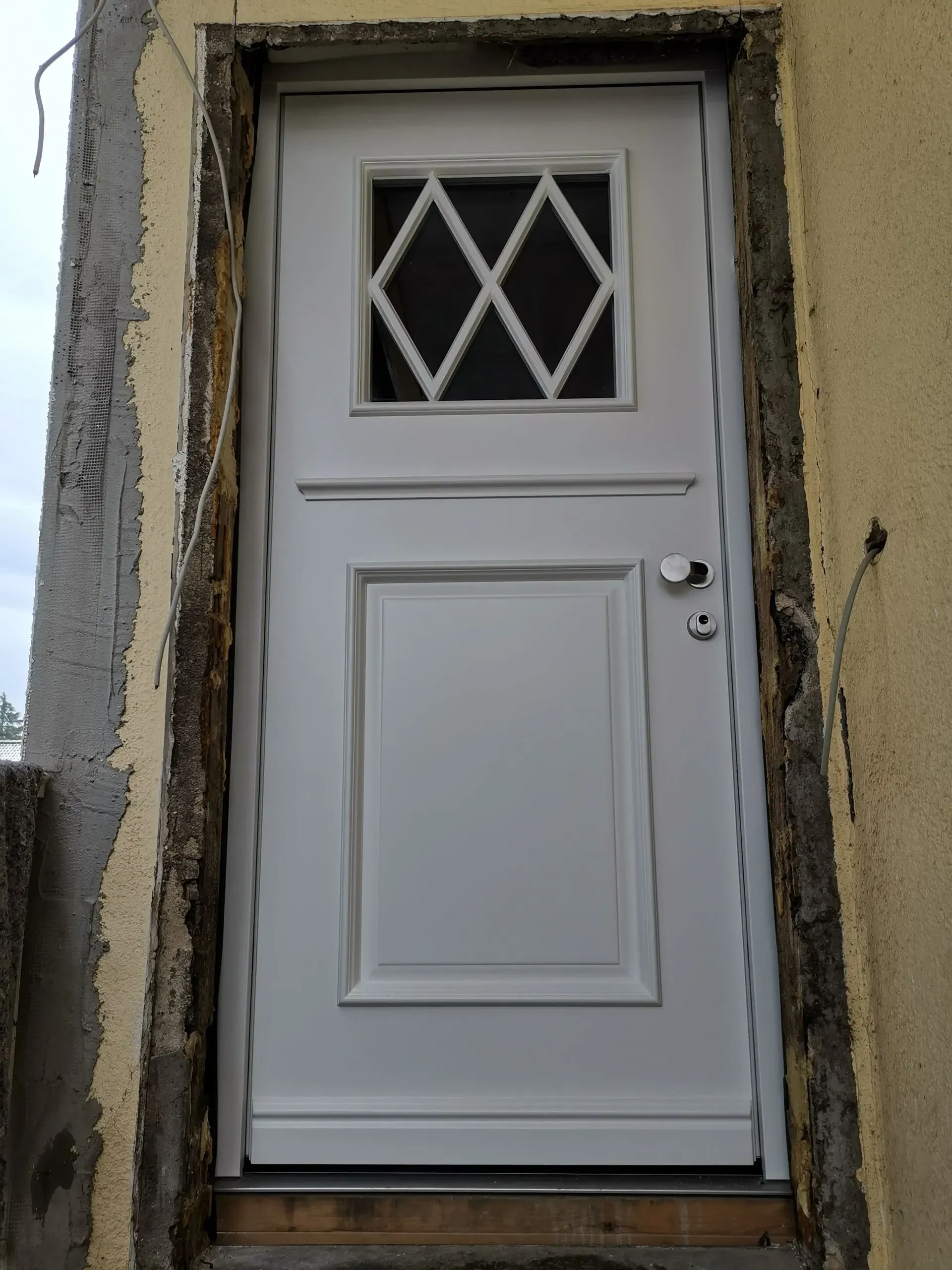 Weiße Haustür mit Rautenverglasung und Kassettenfüllung beim Einbau in einen Altbau