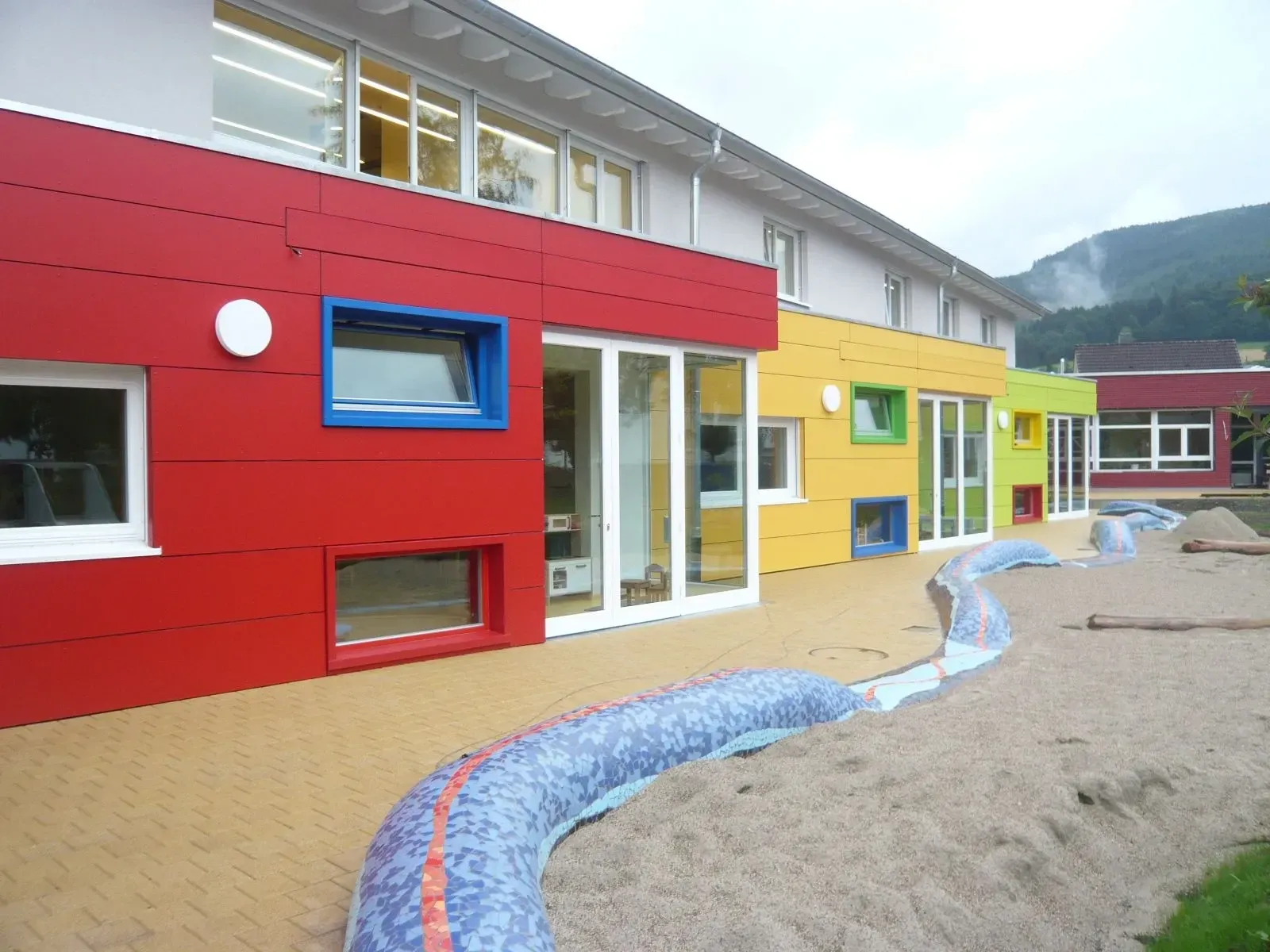 Kindertagesstätte mit farbiger Fassade und Holzfenstern mit farbigen Laibungen