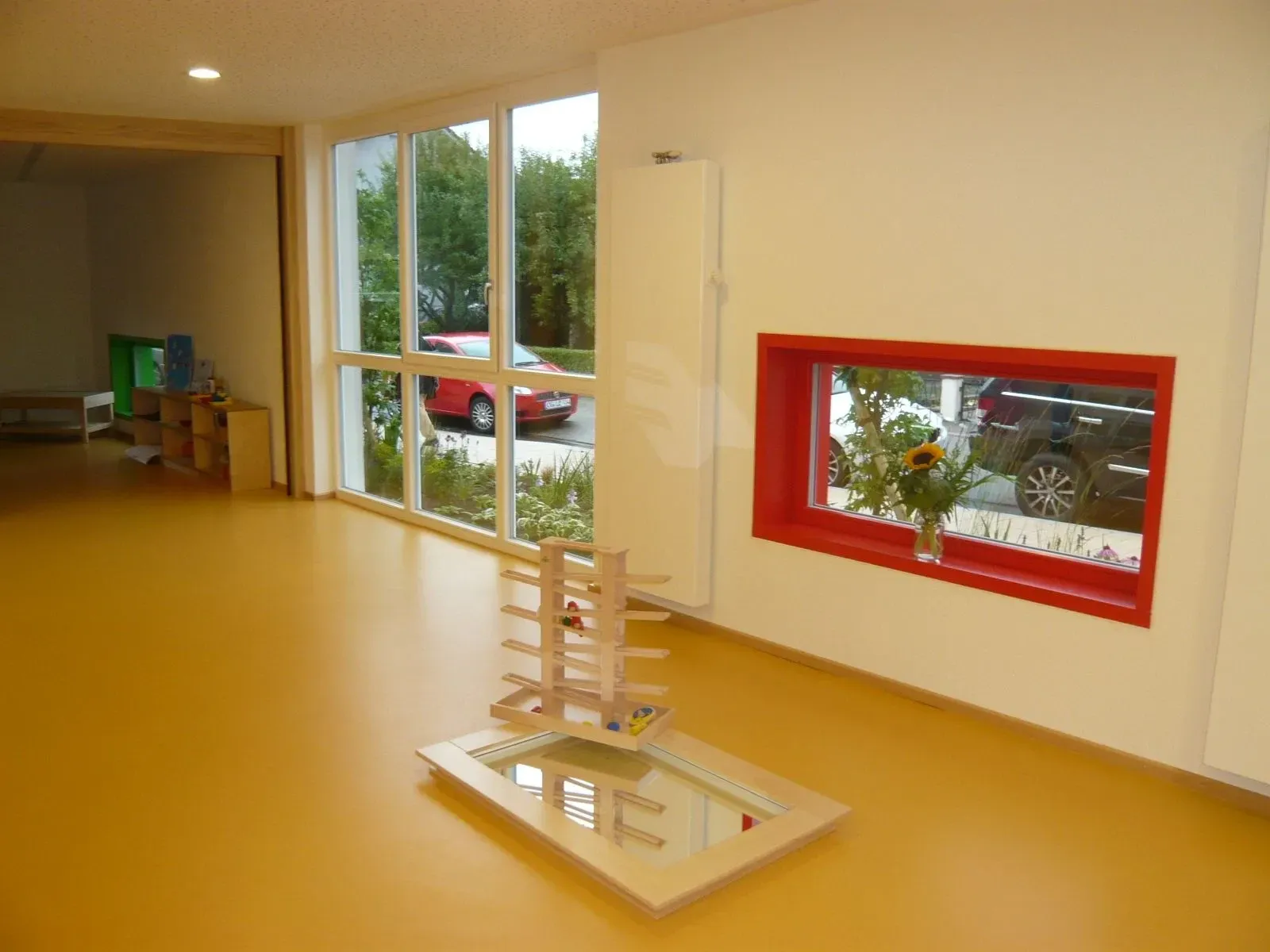 Heller Innenraum mit raumhoher Verglasung und rot eingefasstem Fenster