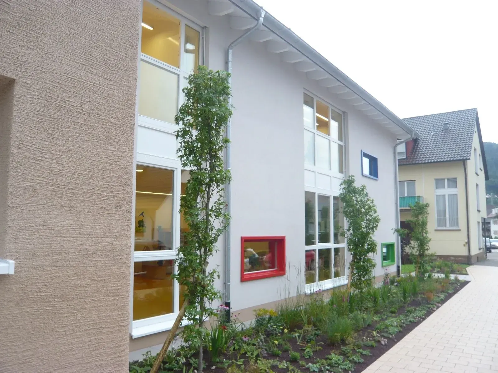 Neubau mit großen Holzfenstern und farbigen Fensterrahmen, Außenansicht