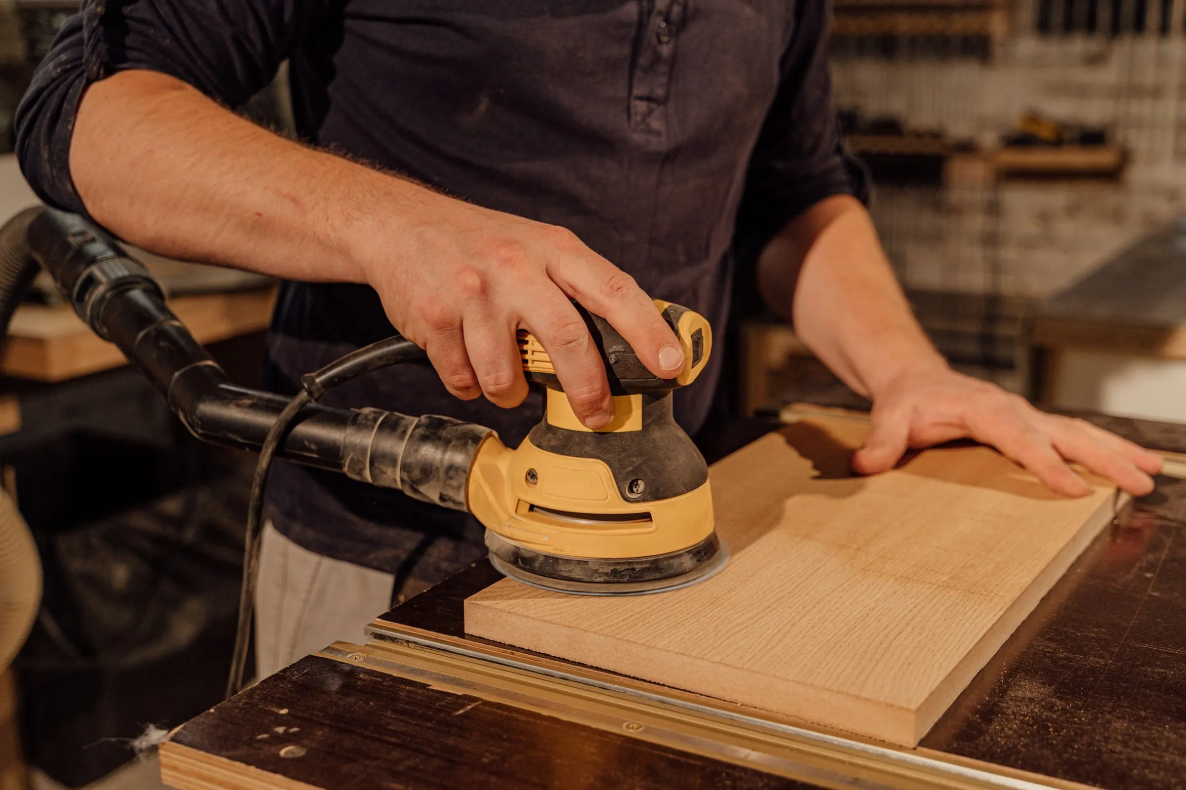 Handwerker schleift ein helles Holzbrett mit dem Exzenterschleifer